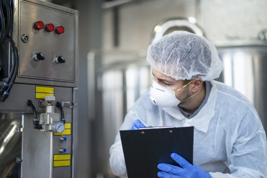 Young technologist in white protective uniform controlling industrial machine at production plant